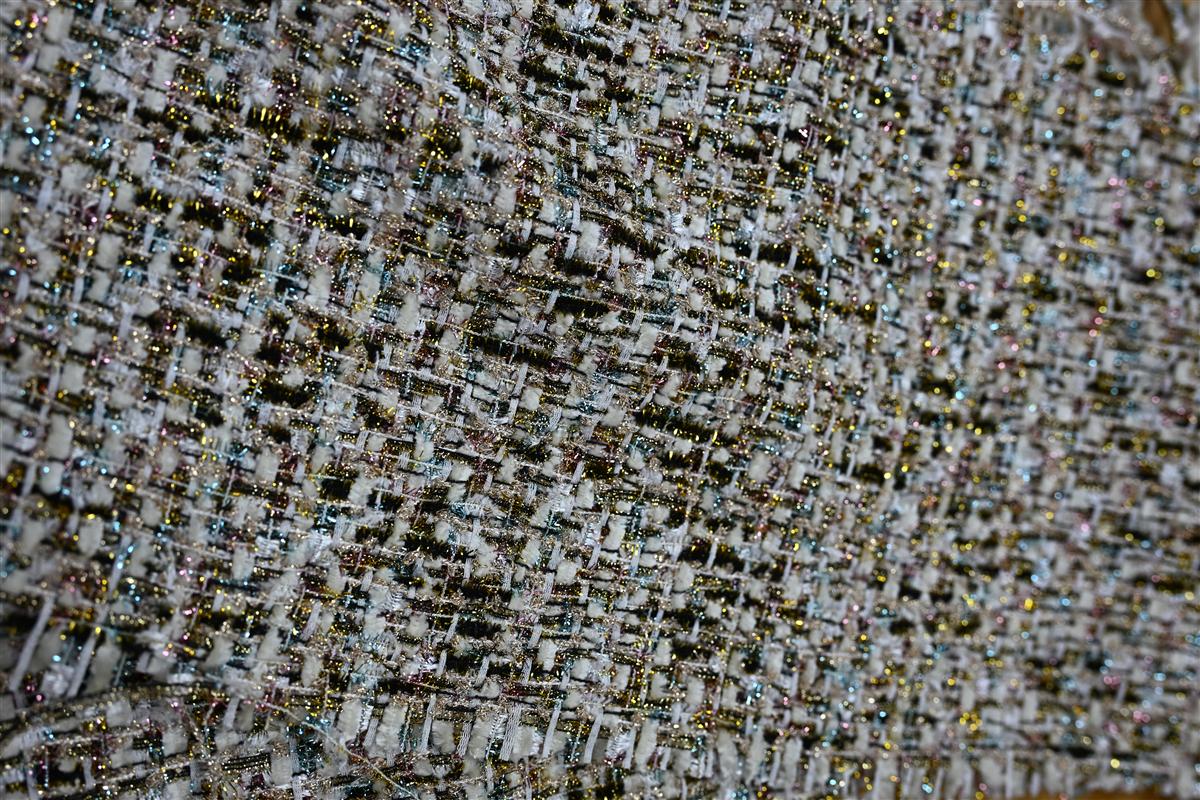 Detailed macro image of premium Chanel-style boucl fabric with intricate woven texture and glittery threads, representing Fursones heritage cable knits and bespoke fabric development. This photo highlights our expertise in luxury tweed and knit sourcing with 100m ready stock and custom MOQ solutions.