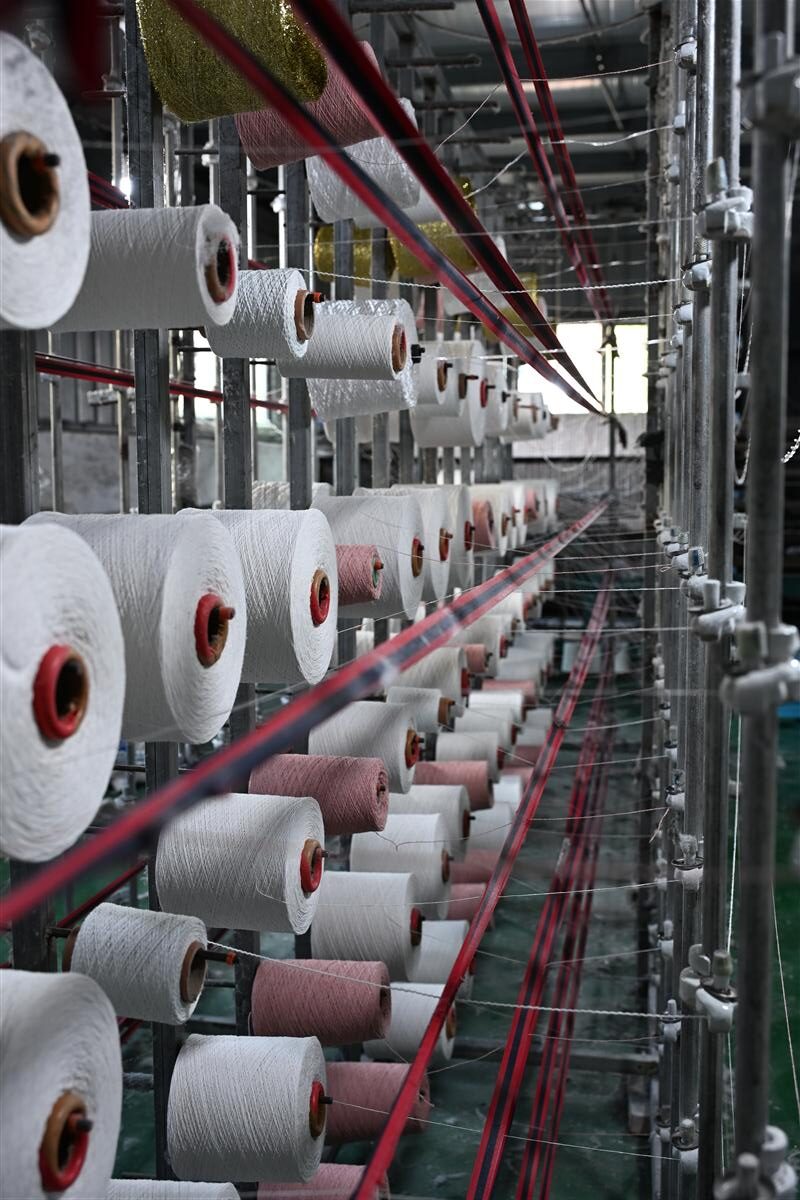 Rows of white and colored yarn spools organized in a textile manufacturing facility, illustrating Fursone's expertise in sourcing tweed fabric from Wenzhou. This image highlights our premium European-quality yarns ready for rapid sampling, 3-7 day shipping, and custom bespoke fabric development.