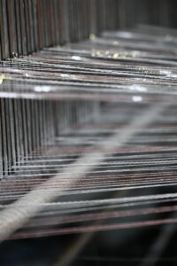 Close-up image of intricate yarn threads on a textile loom, representing the precision and artisan quality of Wenzhou textile expertise. This detailed view highlights our core product of sourcing tweed fabric from Wenzhou, emphasizing premium quality and craftsmanship suitable for Chanel-style bouclé and heritage cable knits.