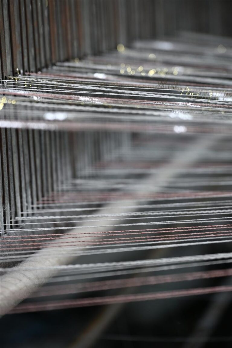 Close-up image of intricate yarn threads on a textile loom, representing the precision and artisan quality of Wenzhou textile expertise. This detailed view highlights our core product of sourcing tweed fabric from Wenzhou, emphasizing premium quality and craftsmanship suitable for Chanel-style bouclé and heritage cable knits.