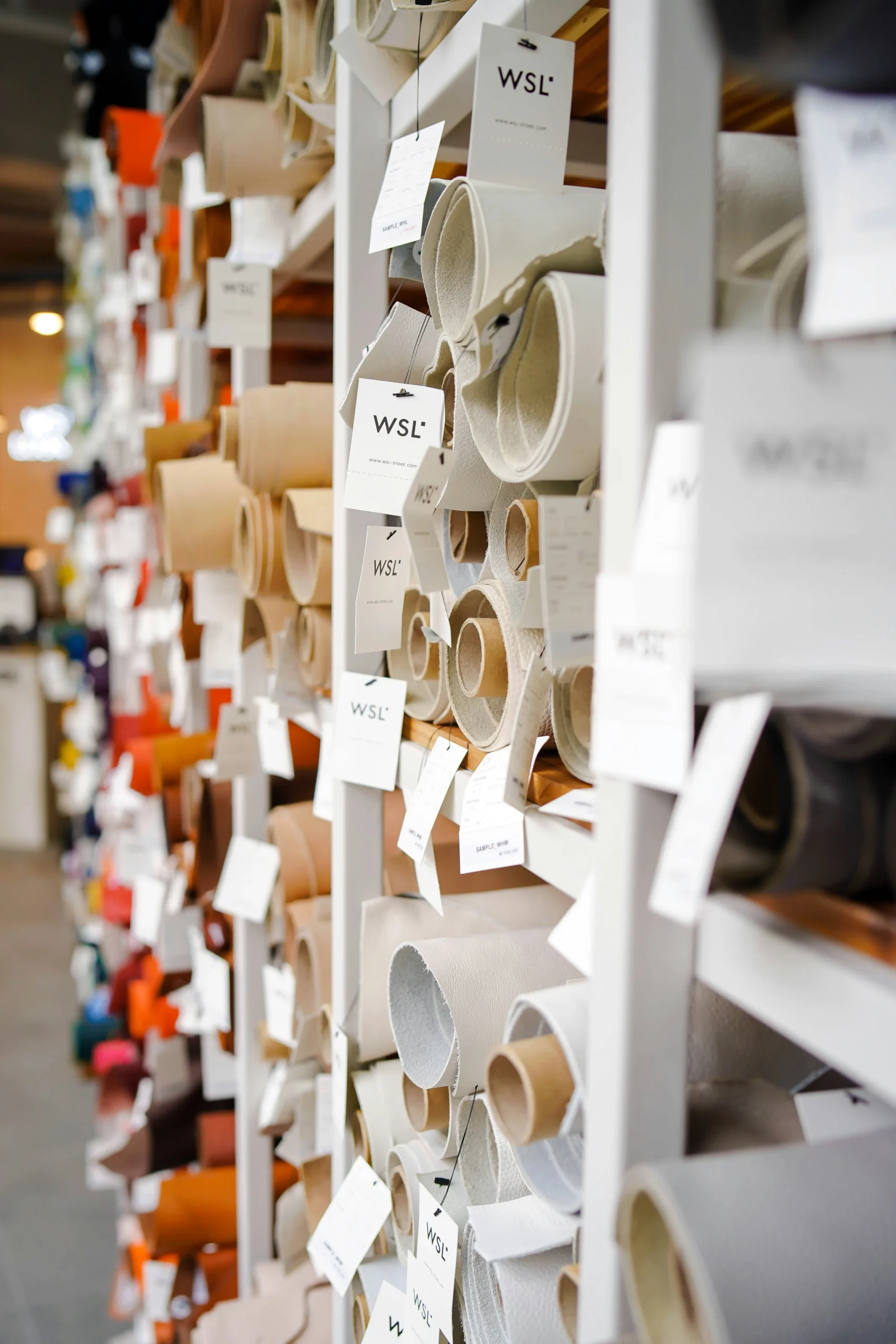 Wall of neutral fabric rolls on shelving, illustrating Fursone's Ready Stock Fabric offering for quick 3–7 day shipping. It reflects our Wenzhou textile expertise in premium tweed and knit textures for luxury brands.