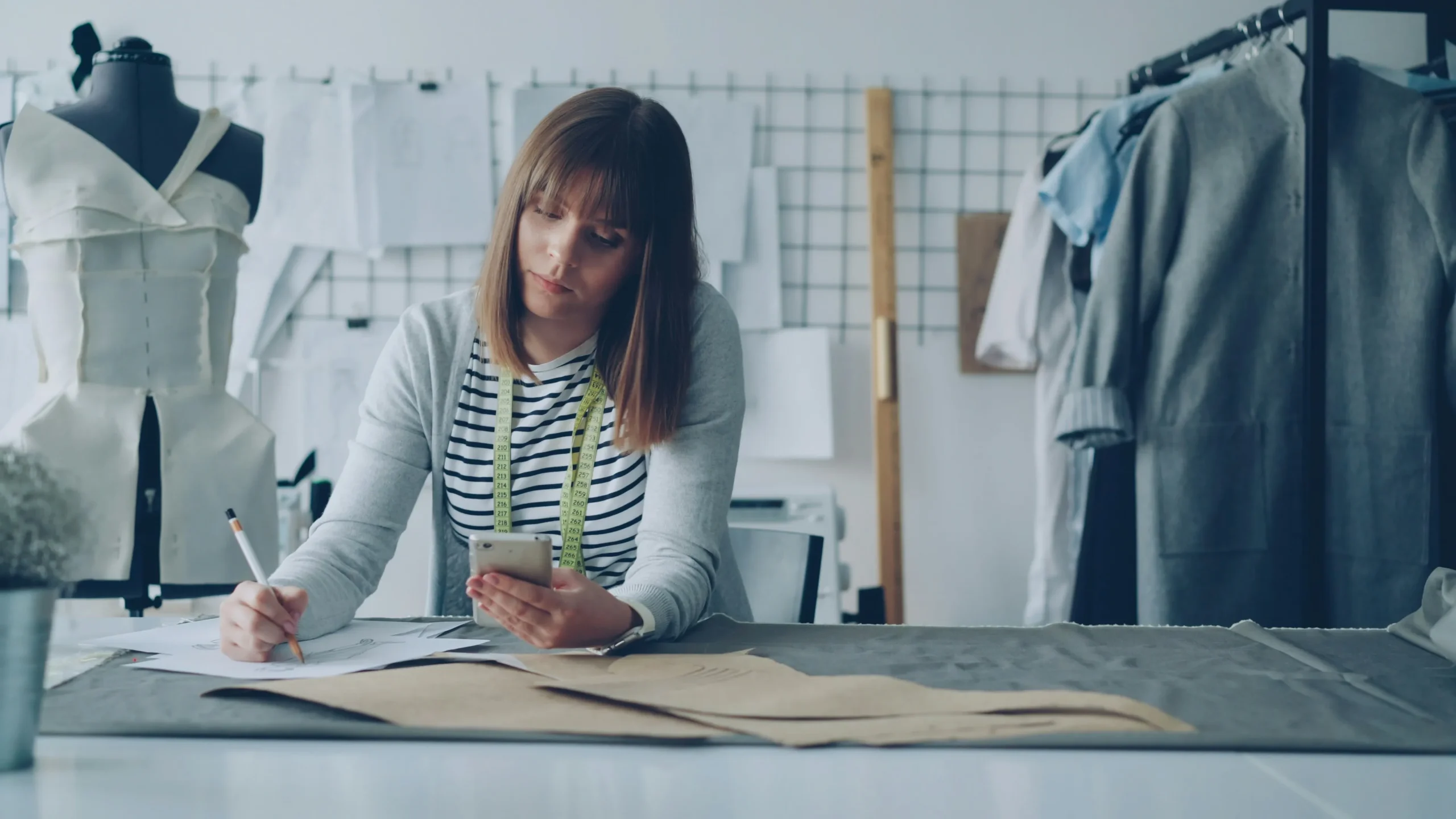 Inside a fashion studio, a designer at Fursone reviews sketches and fabric swatches with a measuring tape. This scene embodies Rapid Sampling: 7-Day Turnaround for Fabric Development for Chanel-style bouclé, tweed, and heritage knit fabrics.