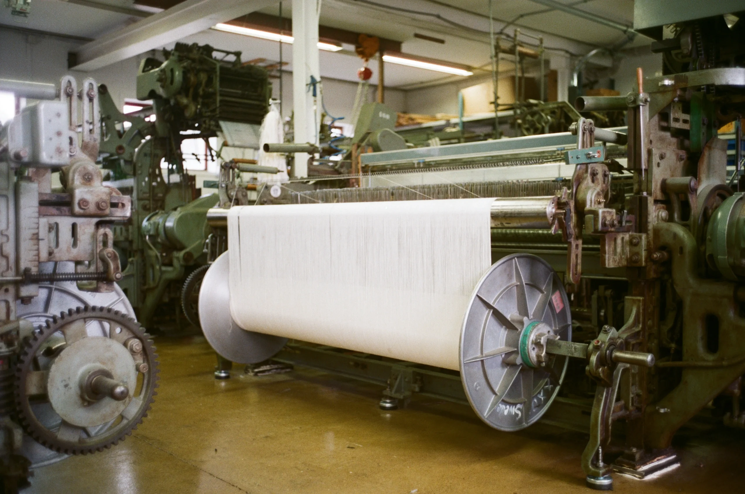 Industrial textile factory scene showing a large fabric roll on a knitting/loom line, representing Fursone’s Heritage Cable Knits production and knit fabric manufacturing. From Wenzhou textile expertise since 1995, we offer premium tweed and bouclé fabrics with ready stock and bespoke options.