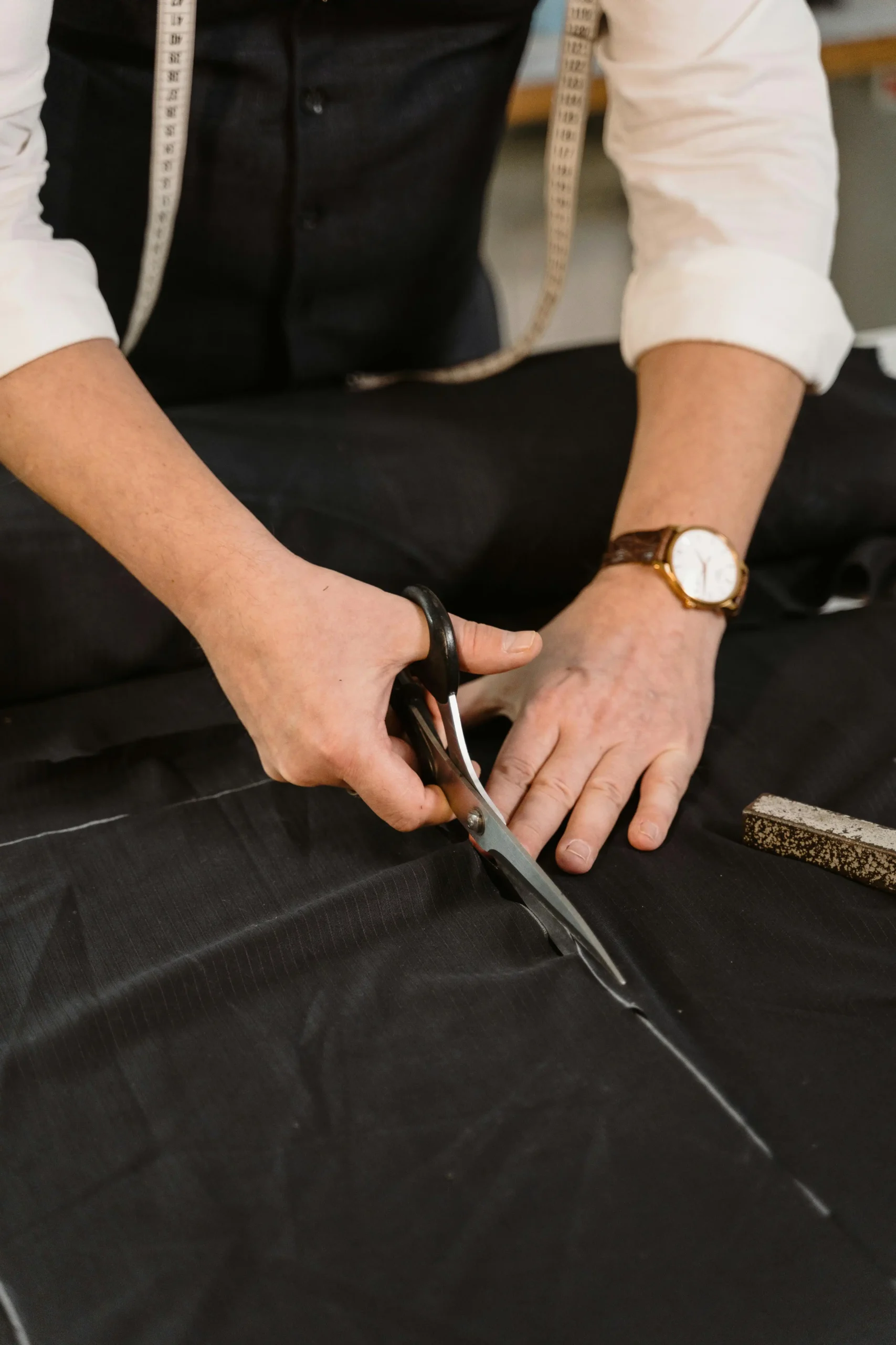 A craftsman cuts premium black fabric with scissors on a worktable, illustrating Fursone's Custom Bespoke Fabric Development from concept to roll. The scene reflects our Wenzhou textile expertise in premium tweed and knit fabrics for luxury brands.