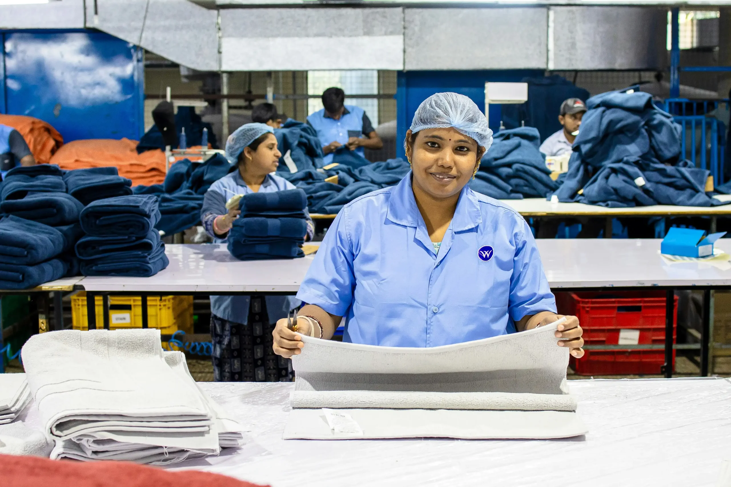 A Fursone technician inspects Chanel-Style Boucl Fabric on a production table, with stacks of tweed and knit rolls in the background. The scene showcases Wenzhou textile expertise and capabilities in ready stock and rapid fabric development for premium collections.