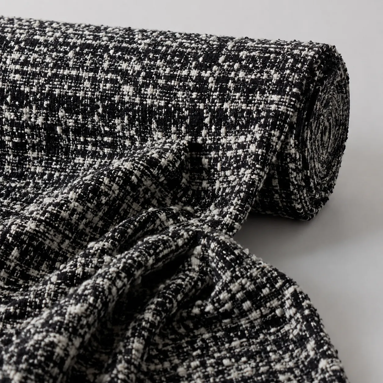 Hyper-realistic product photography, a luxurious roll of Chanel-style boucl fabric in black and white tweed texture, soft studio lighting, fabric draped elegantly, hyper-detailed fiber loops, clean background, no text, no brand logo
