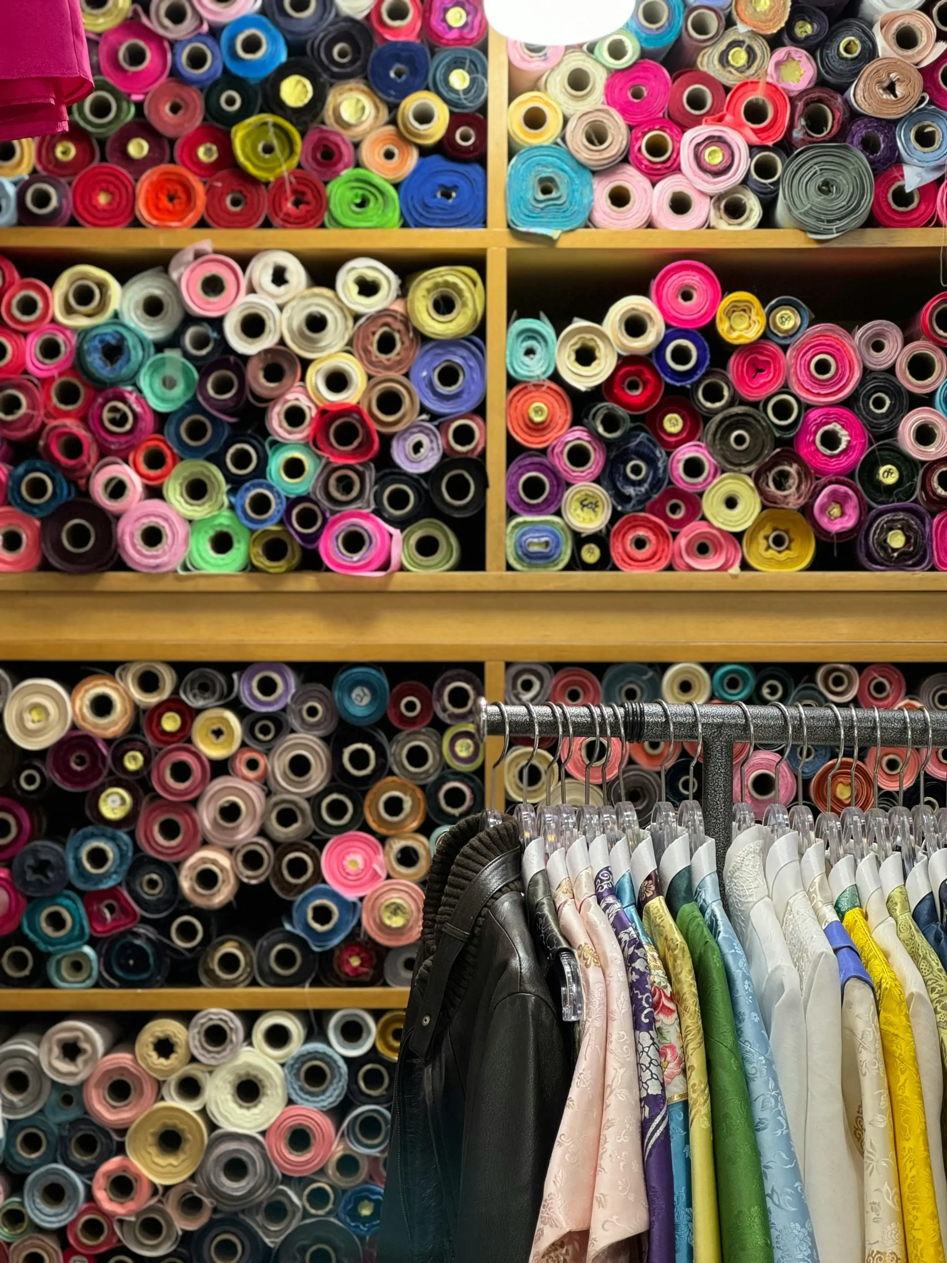 Colorful rolls of Ready Stock Fabric line the shelves in a Fursone showroom, illustrating fast-access inventory for Chanel-style bouclé, heritage tweed, and knit fabrics. This image embodies Fursone's Wenzhou textile expertise and readiness to ship for rapid collection development.